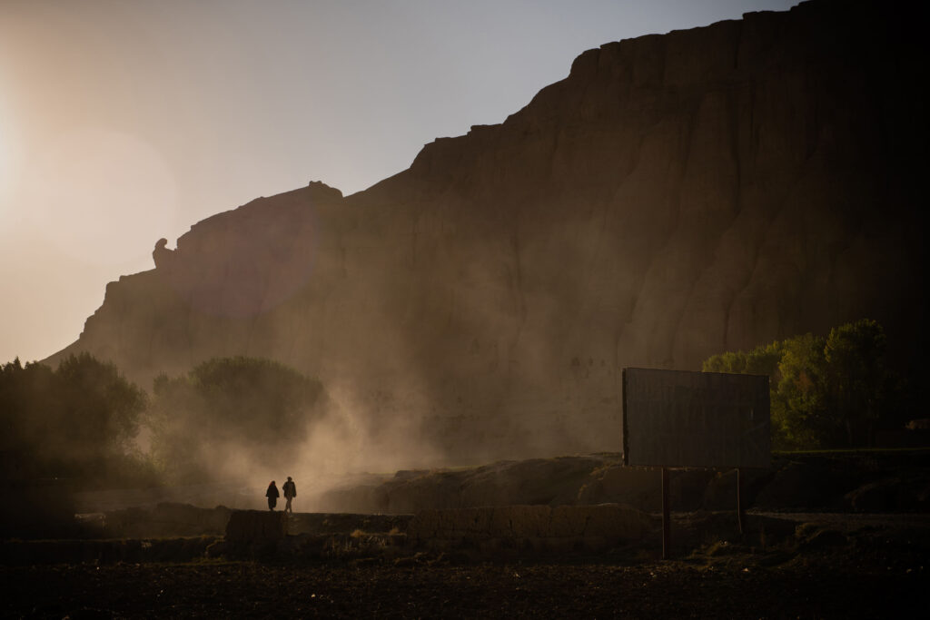 The silhouettes of two people walking in front of vast mountains. 