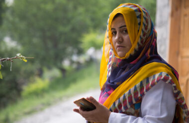 Mufida holds her phone and looks into the camera. She is wearing a colourful headscarf.