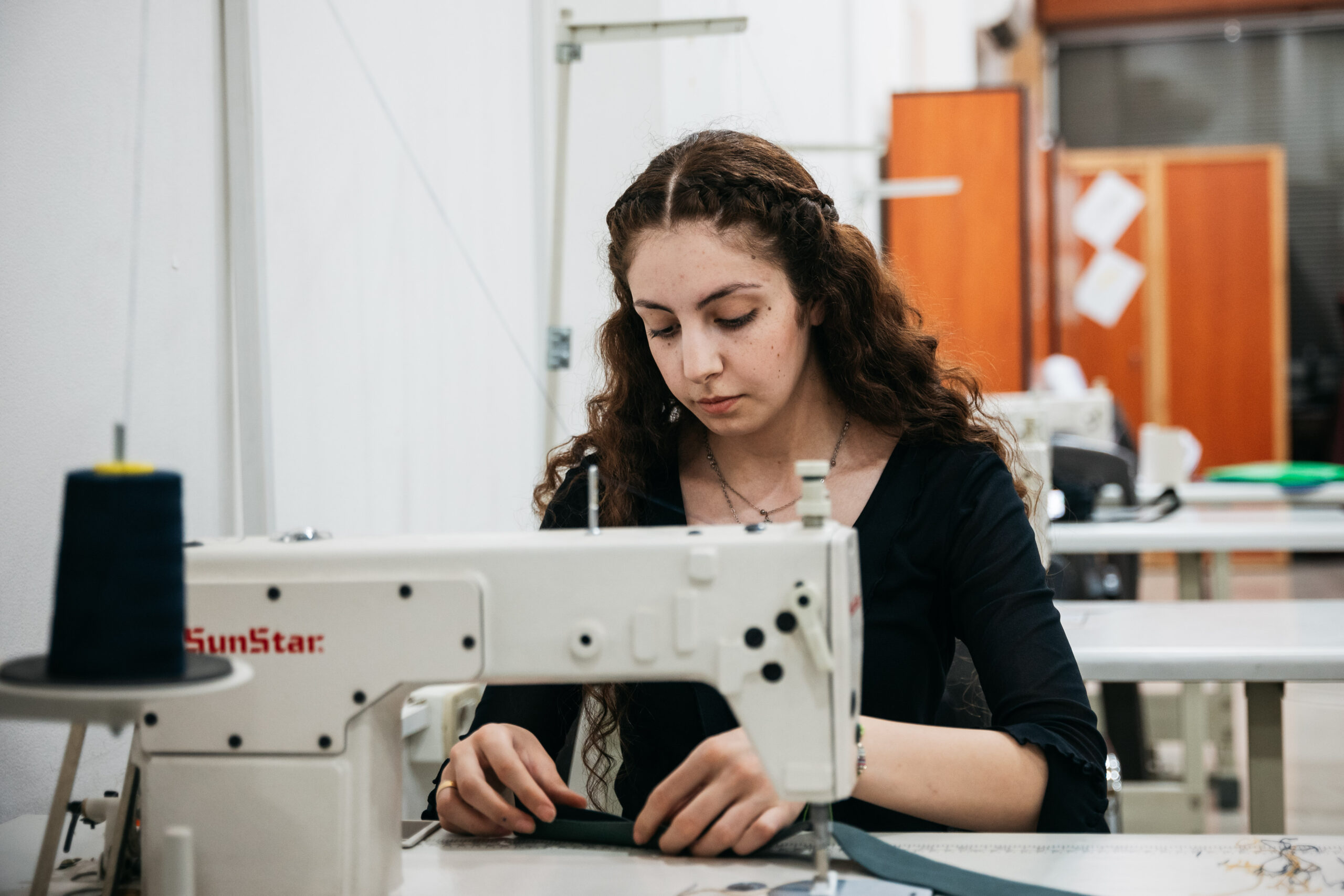 A young woman is mending black fabric with a sewing machine.