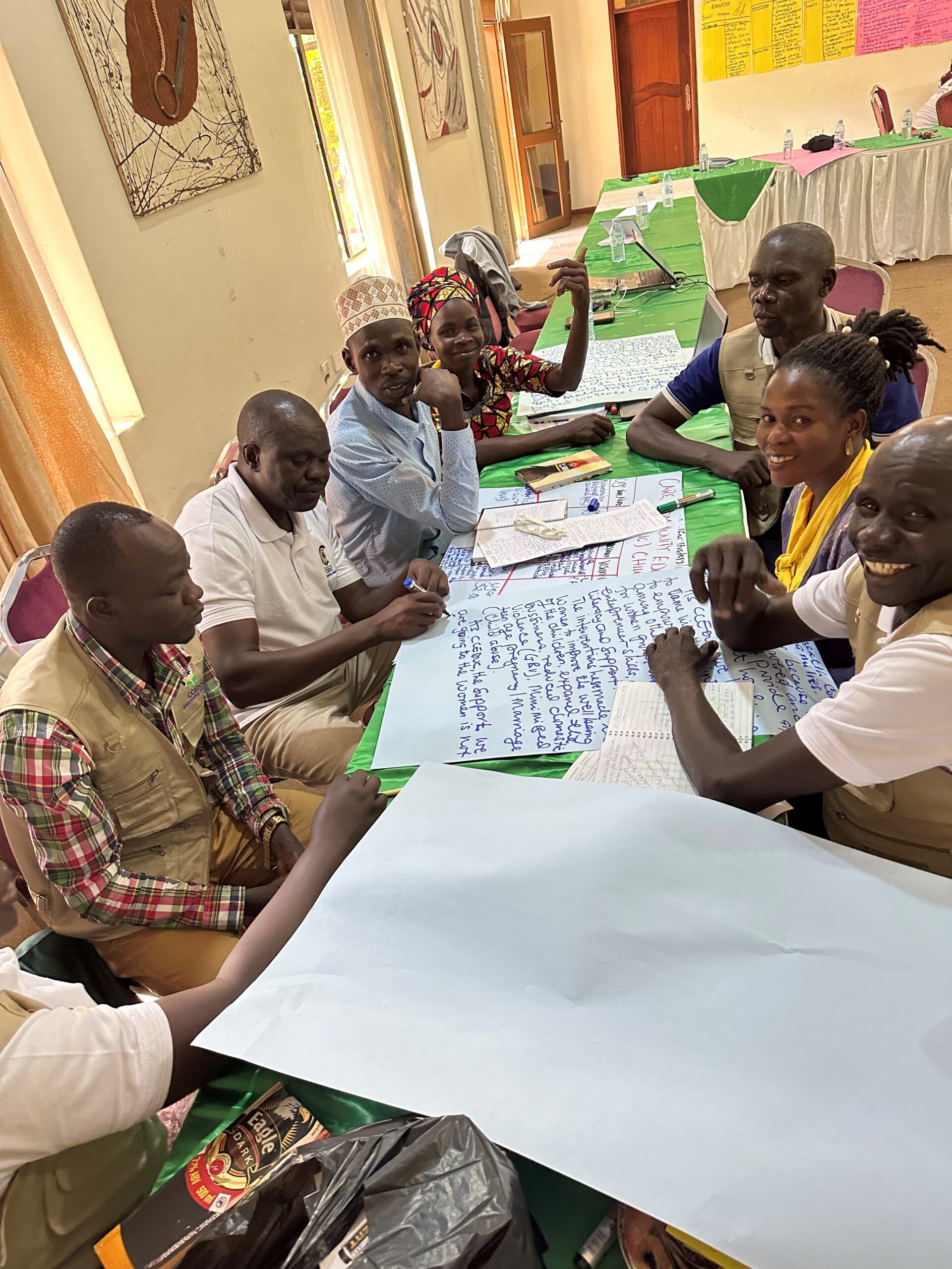 A group of workshop participants are sitting at a table, writing notes in marker on pieces of poster paper.