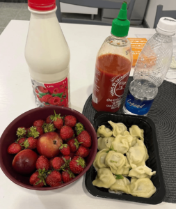 A bowl of strawberries, a tray of dumplings, a water bottle, a bottle of sriracha sauce, and a bottle of raspberry-flavoured yogurt.