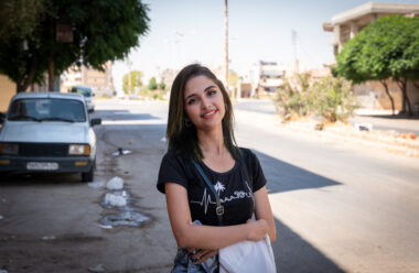 A young woman crosses her arms and smiles at the camera.